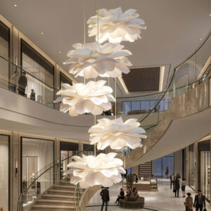 Five white handmade paper flower pendant lights suspended above a luxury staircase. Custom floral chandelier cluster for tall foyer and high ceiling lighting.